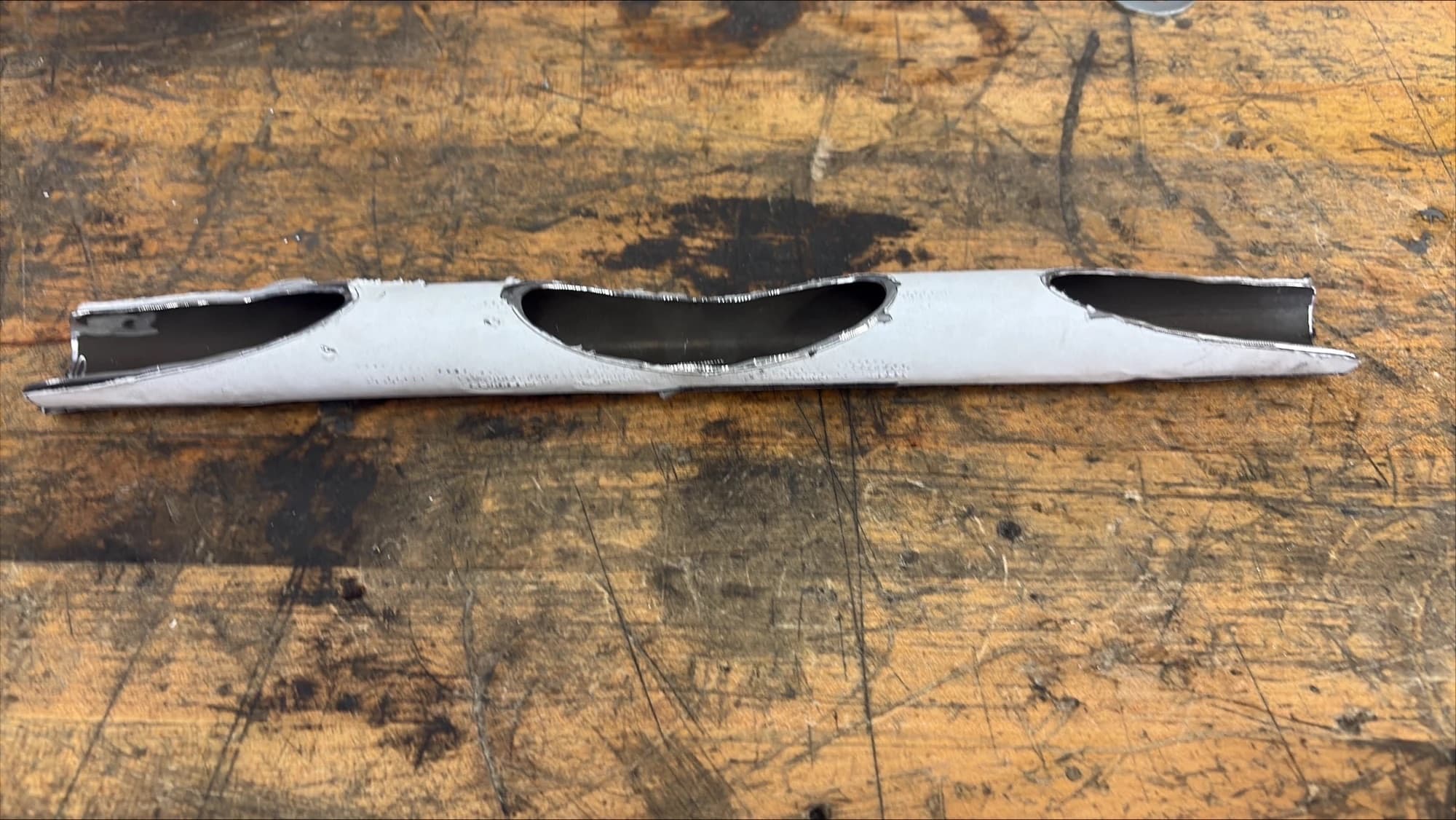 steel tube on a workbench with a paper stencil wrapped on it and three cutouts ground out